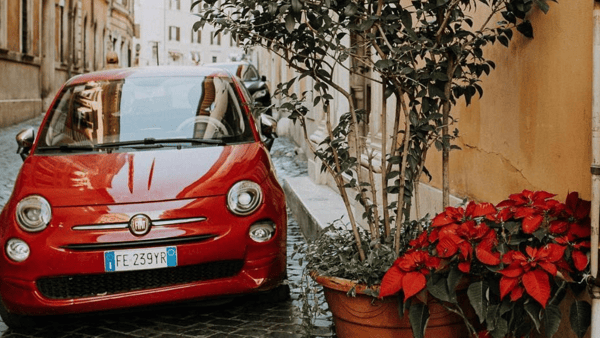 Red Fiat parked on a cobbled street next to red flowers