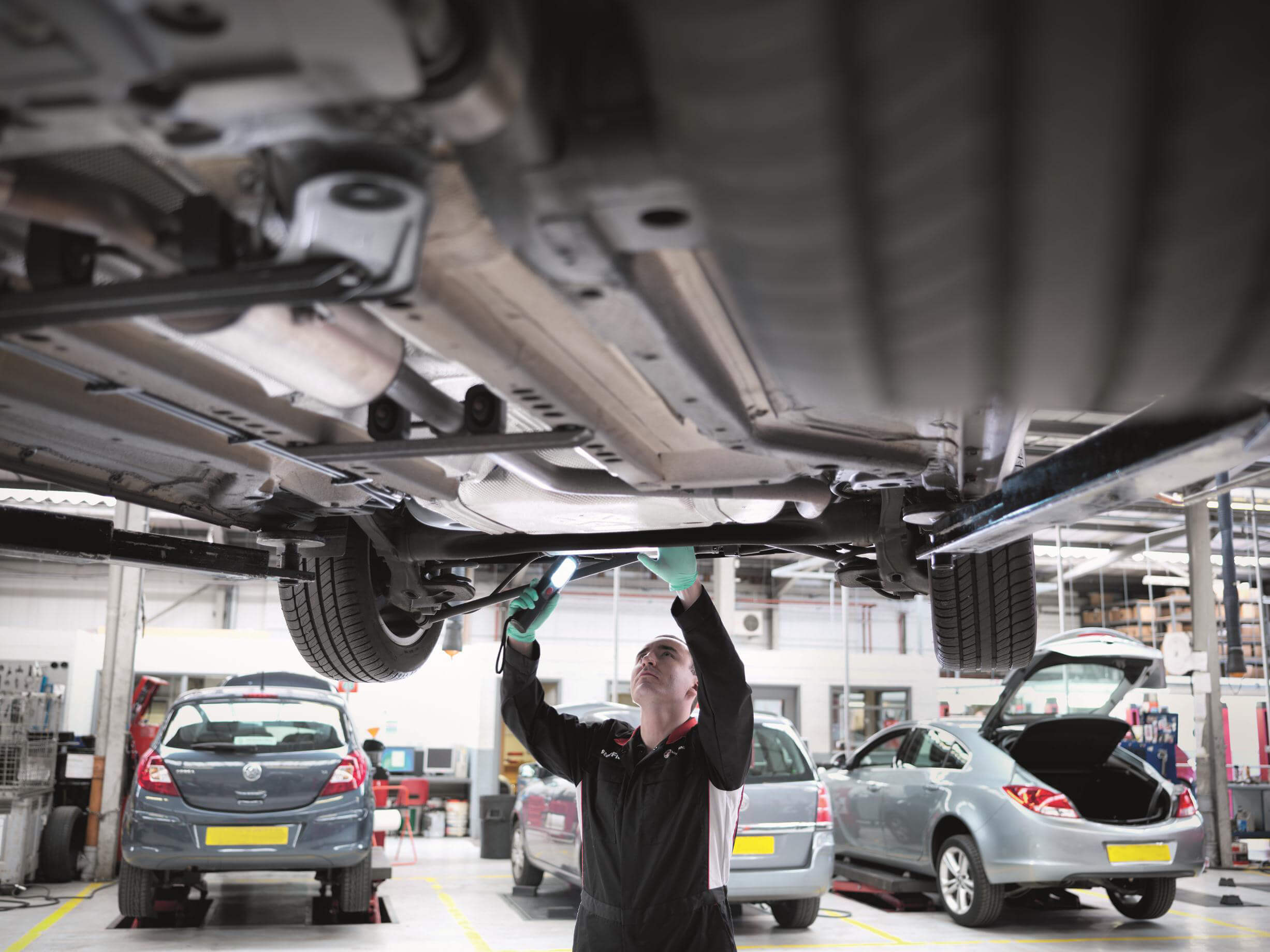 mechanic-inspecting-underside-of-car-three-cars-in-background